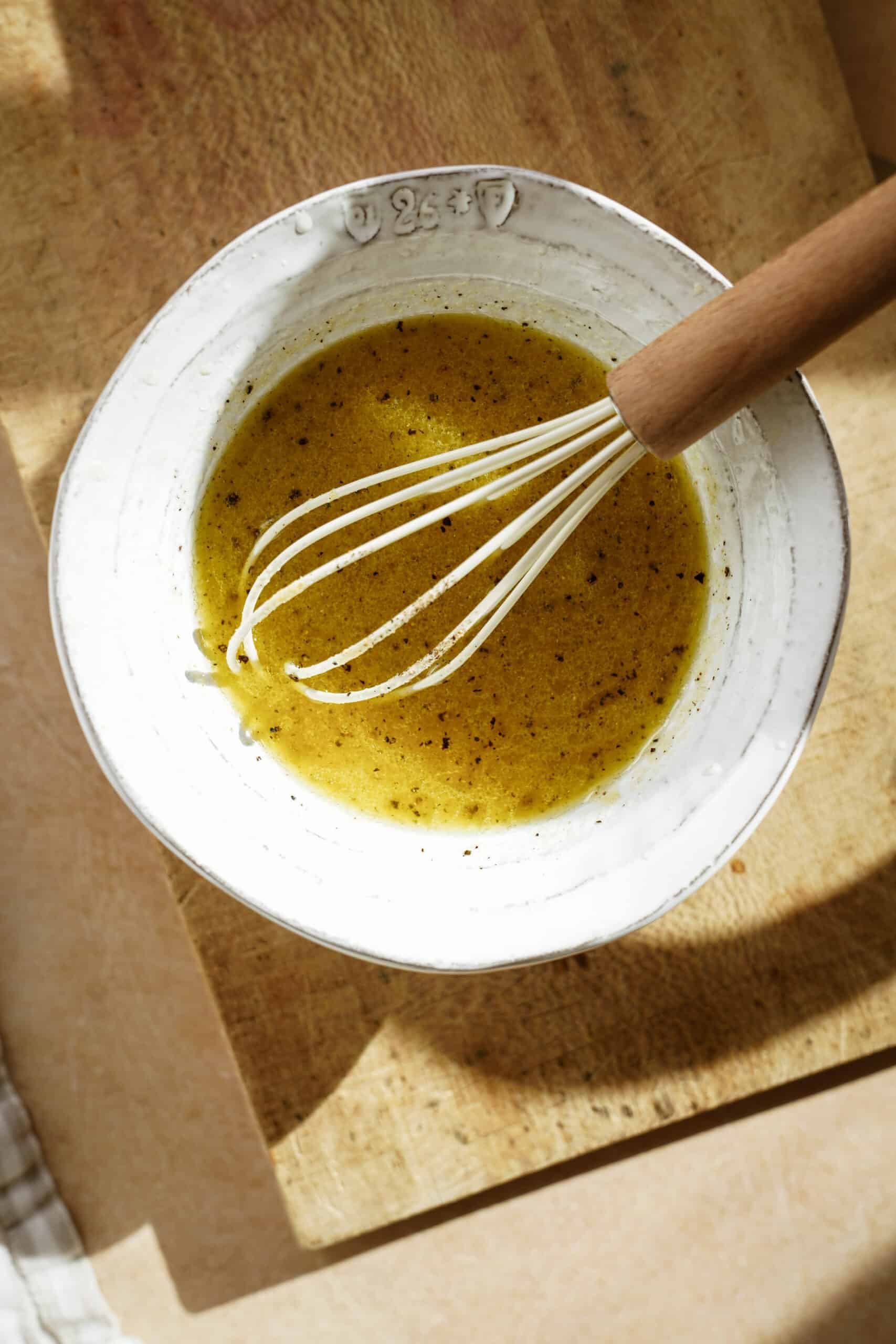 Dressing being mixed with a whisk in a white bowl