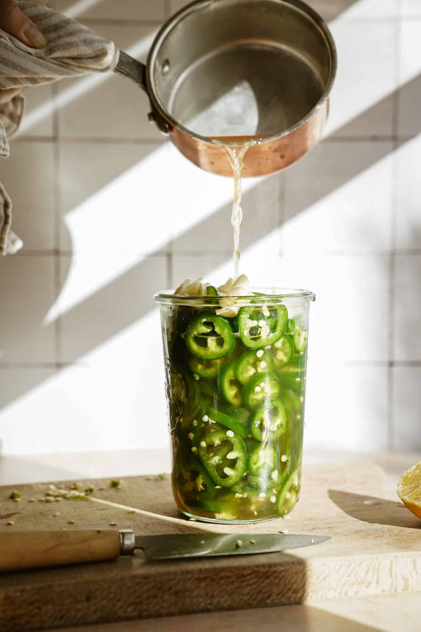 Hot brine being poured over top pickled jalapenos