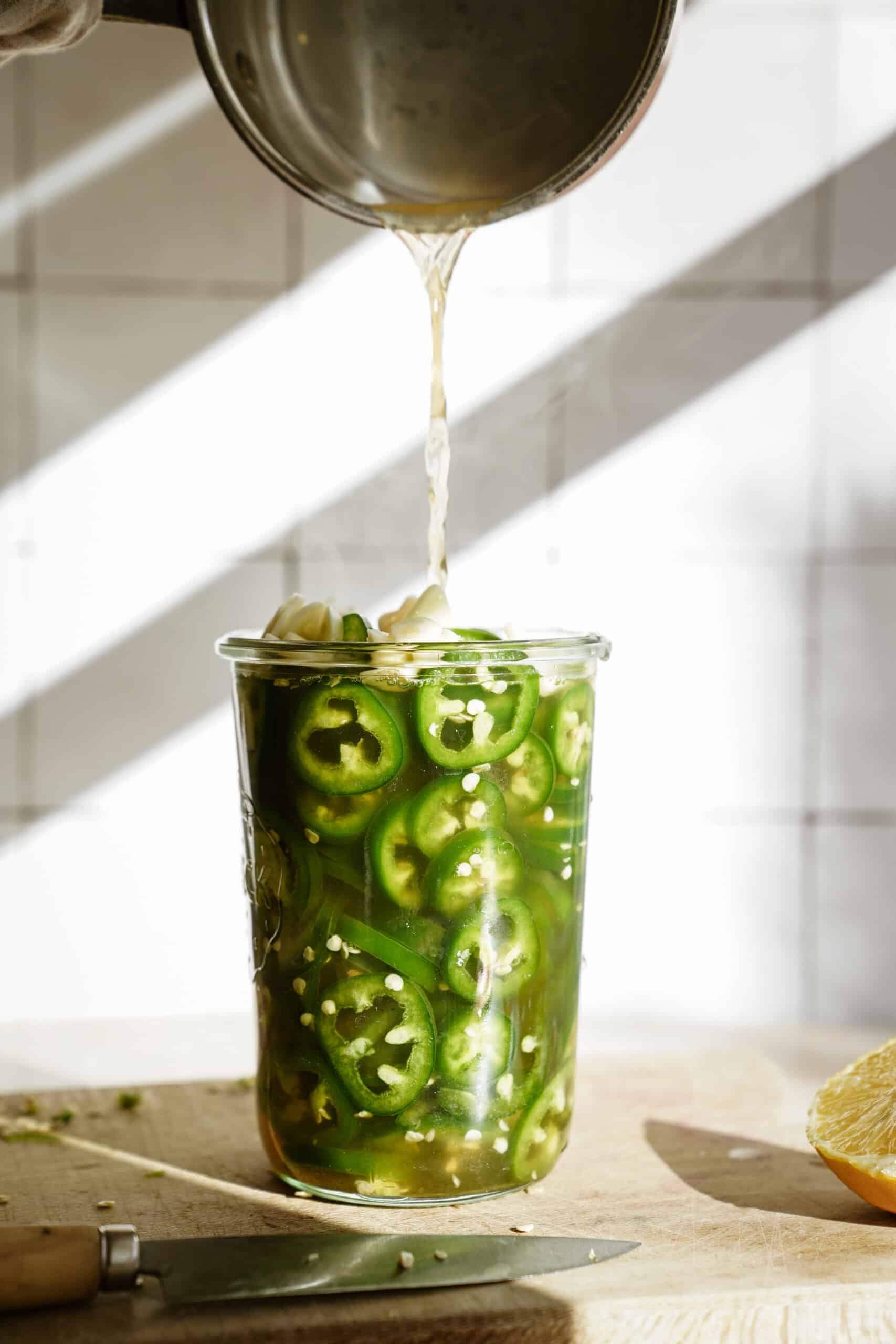 Pouring hot brine on top of pickled jalapenos in a jar
