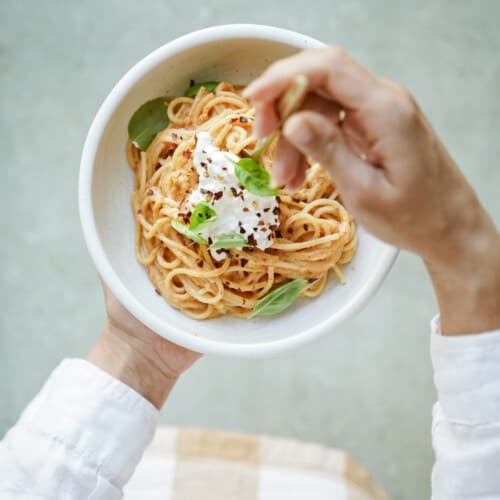Hand swirling burrata pasta in a white bowl