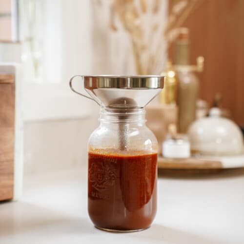 Homemade BBQ sauce being poured into a jar