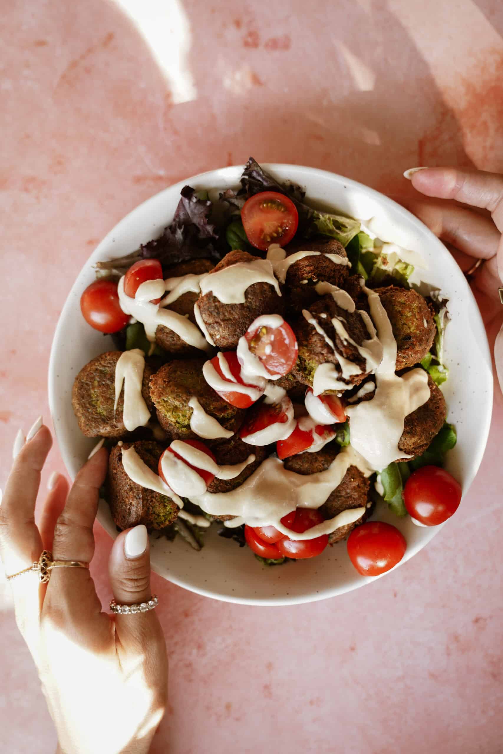 Fresh salad greens and tomatoes with falafel on top and drizzled with tahini sauce