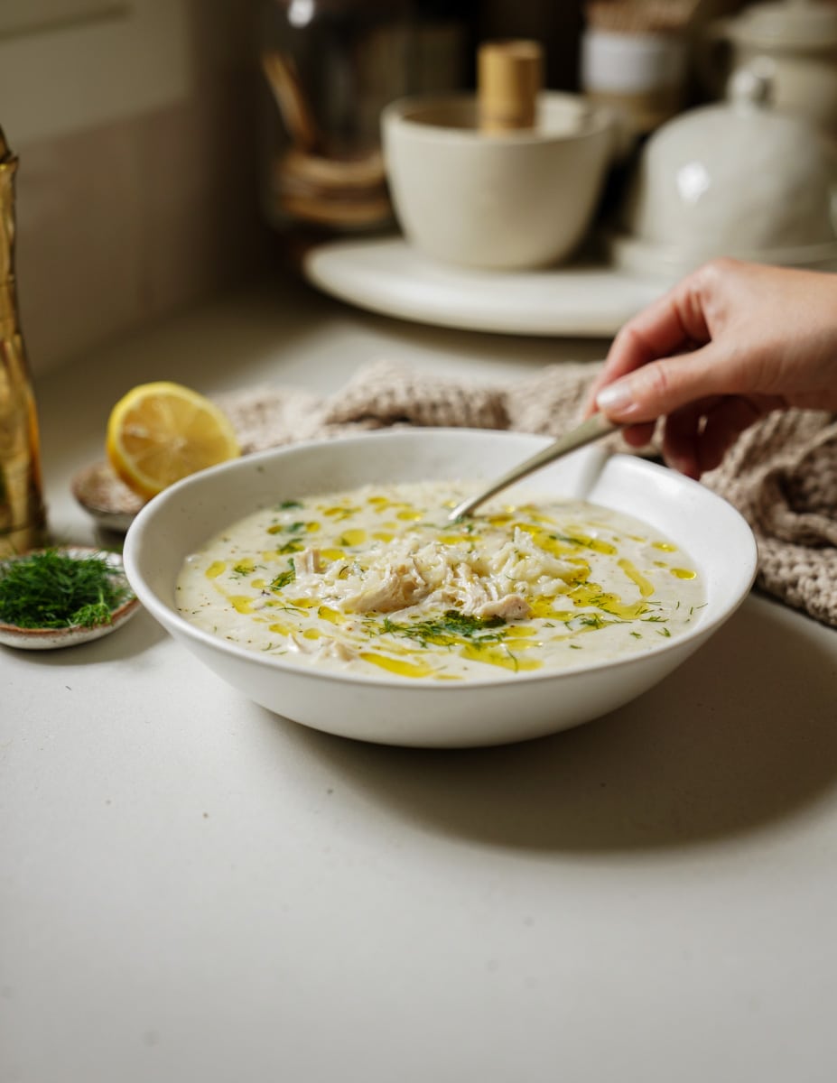 Avgolemono soup in a white bowl with a spoon in it