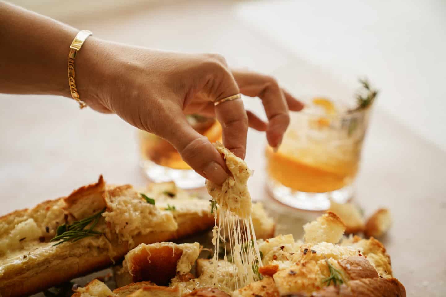 Hand pulling apart cheese bread with cocktail in the back