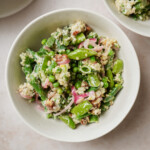 Bowl of quinoa salad, artfully blended with spring mix greens, green beans, peas, red onions, and pecans, all tossed in a creamy dressing.