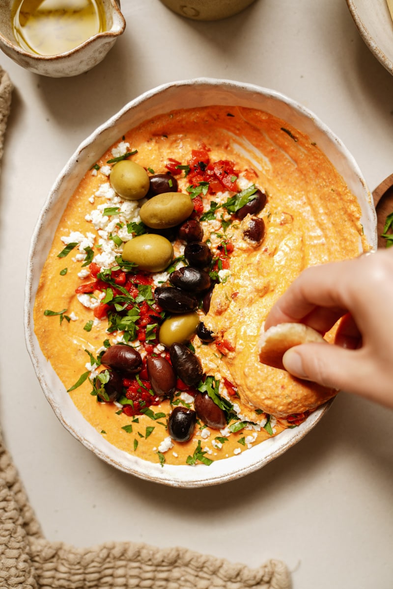 Close up of cracker being dipped in spicy feta dip