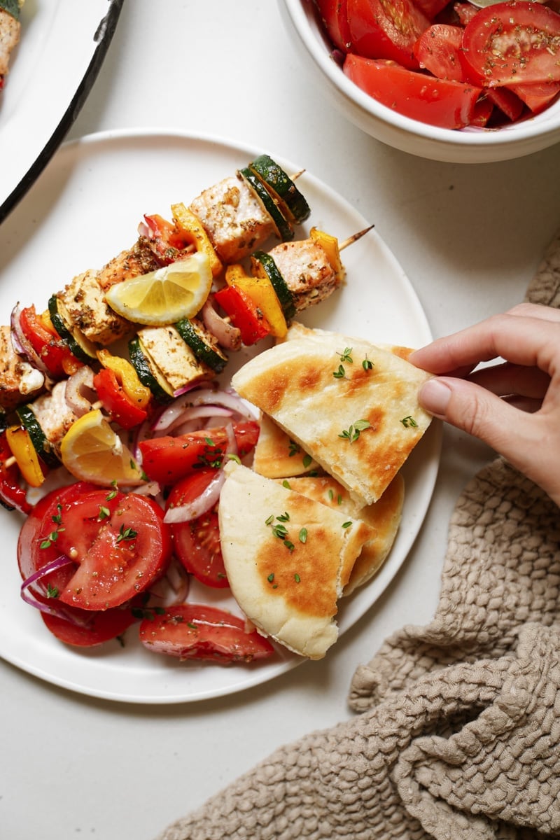 BBQ salmon kebabs on a plate with pita and tomato salad