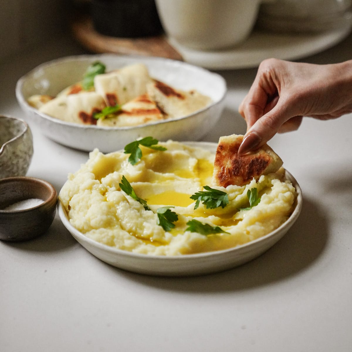 Skordalia in a bowl with bread dipping into it