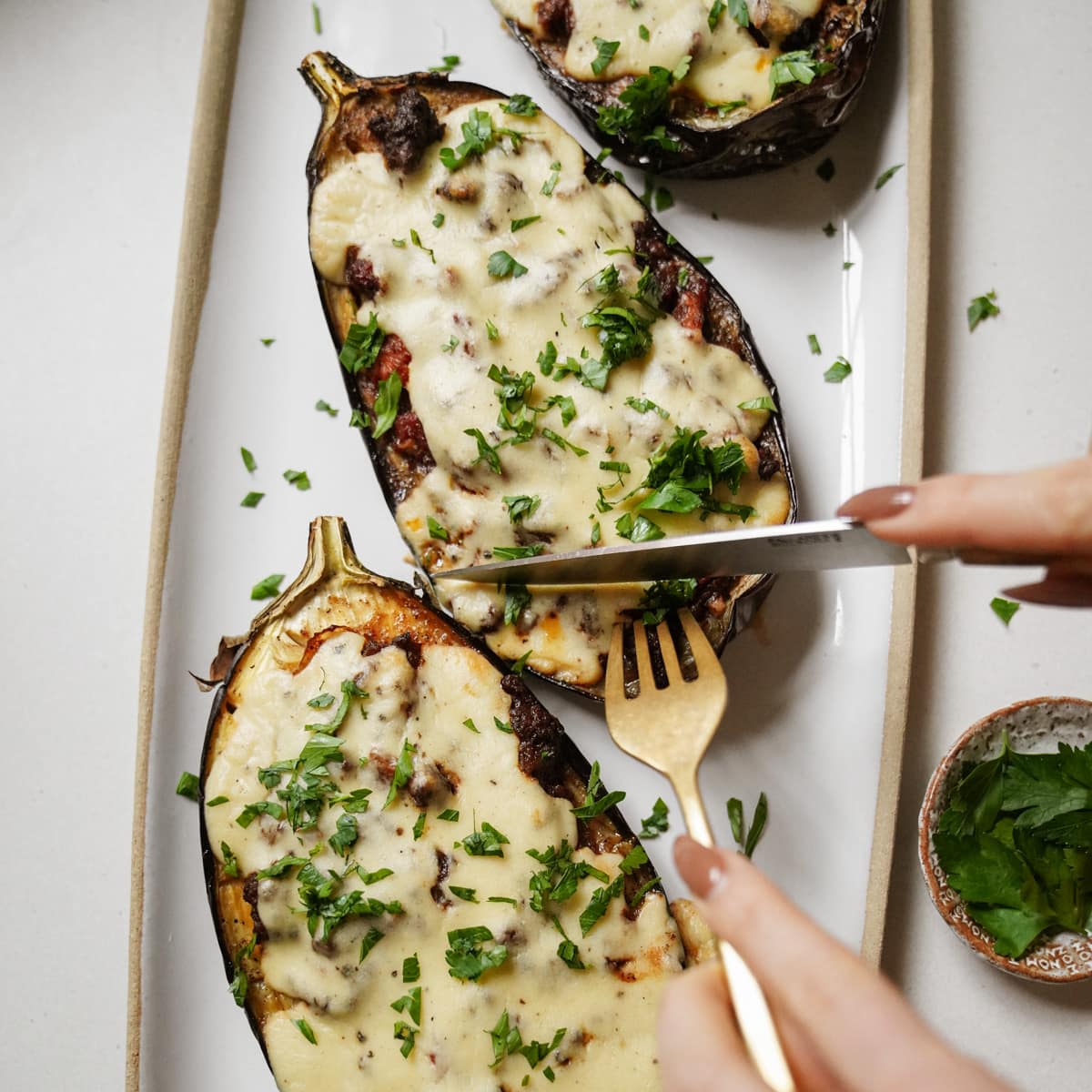 Knife and fork cutting into a stuffed eggplant