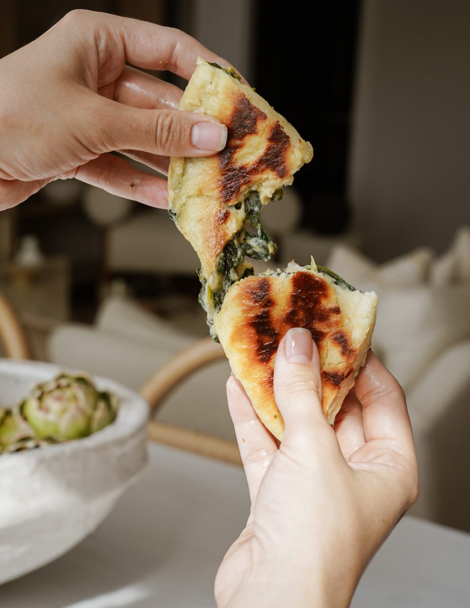 Hand pulling apart a pita bread with spinach in the middle