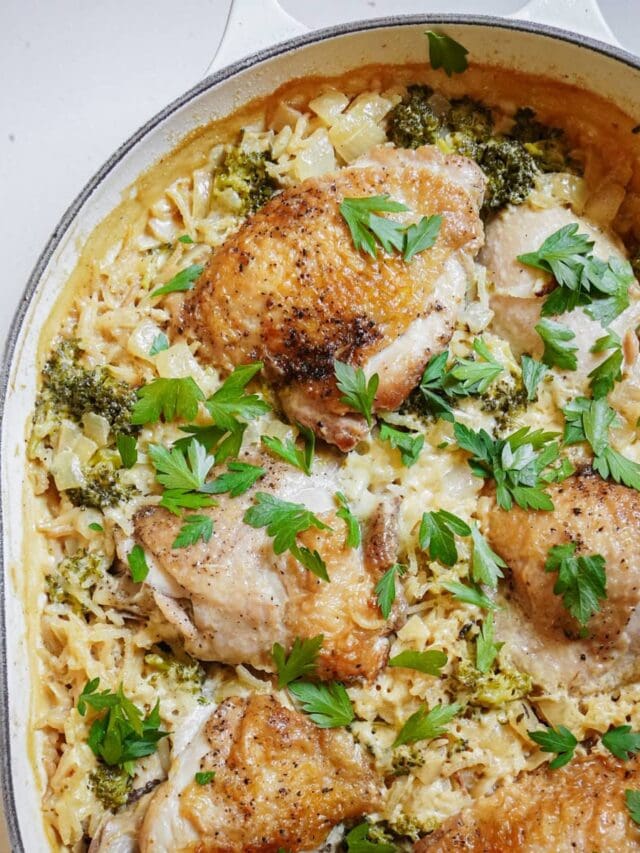 A baked dish with seasoned chicken thighs placed on a bed of rice, broccoli, and creamy sauce. The dish is garnished with fresh parsley.