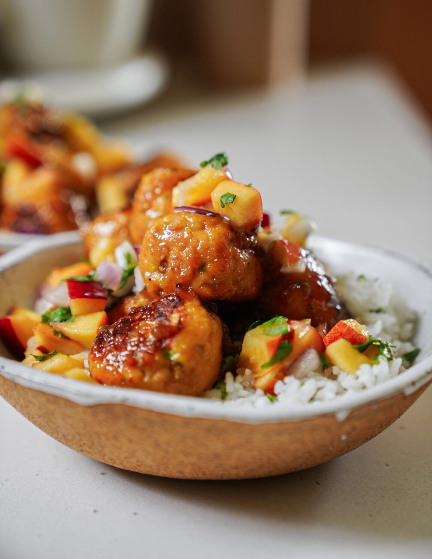 A bowl of white rice topped with browned meatballs and a colorful salsa made from diced peaches, red onions, and fresh herbs.