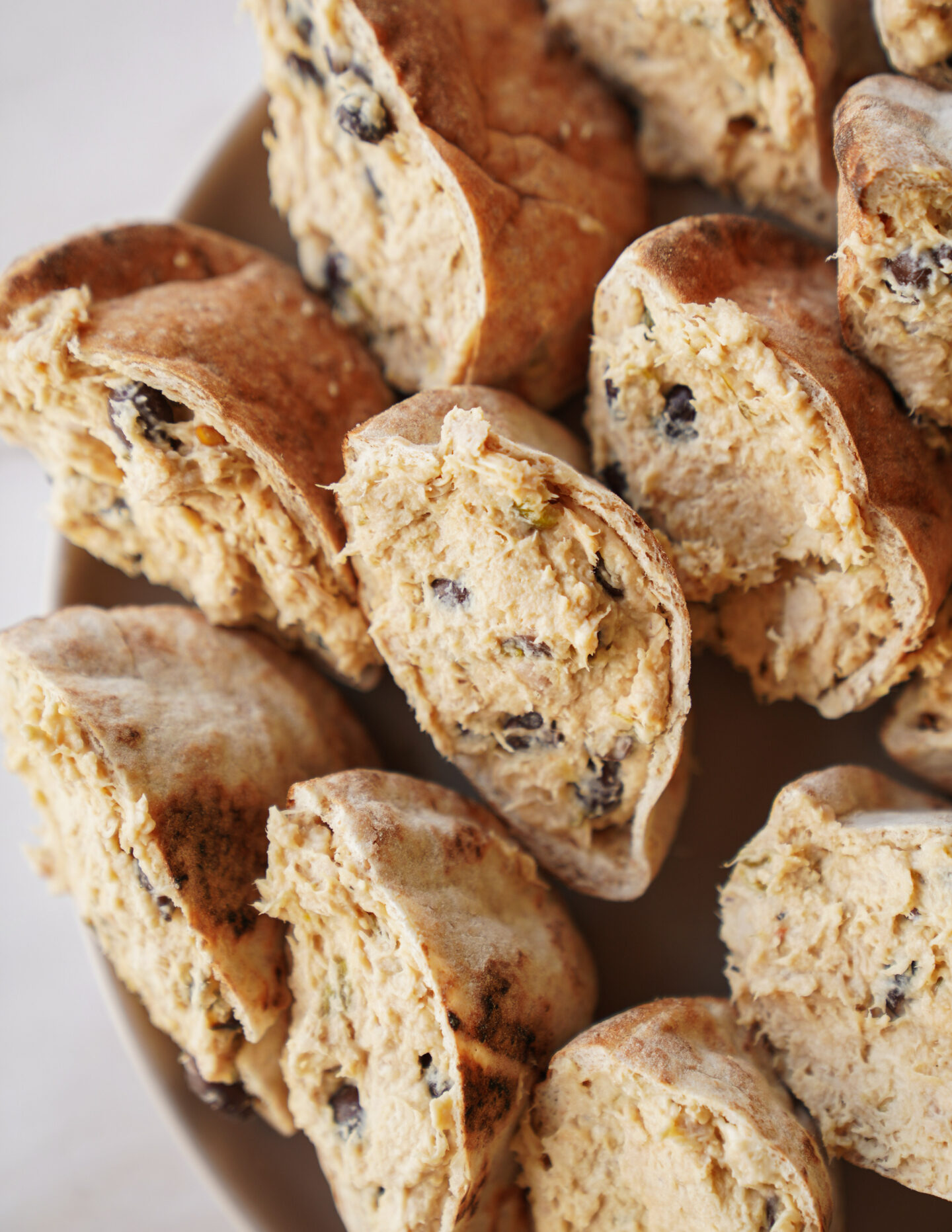 Sliced pieces of bread filled with a creamy mixture containing chocolate chips, arranged closely together on a plate.