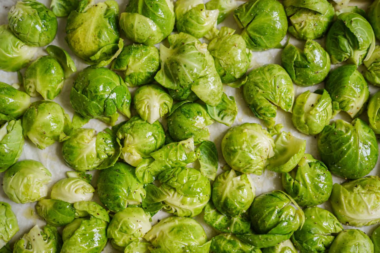 Close-up of fresh Brussels sprouts, halved and whole, scattered on a baking sheet, coated lightly with oil and seasoning, ready for roasting.