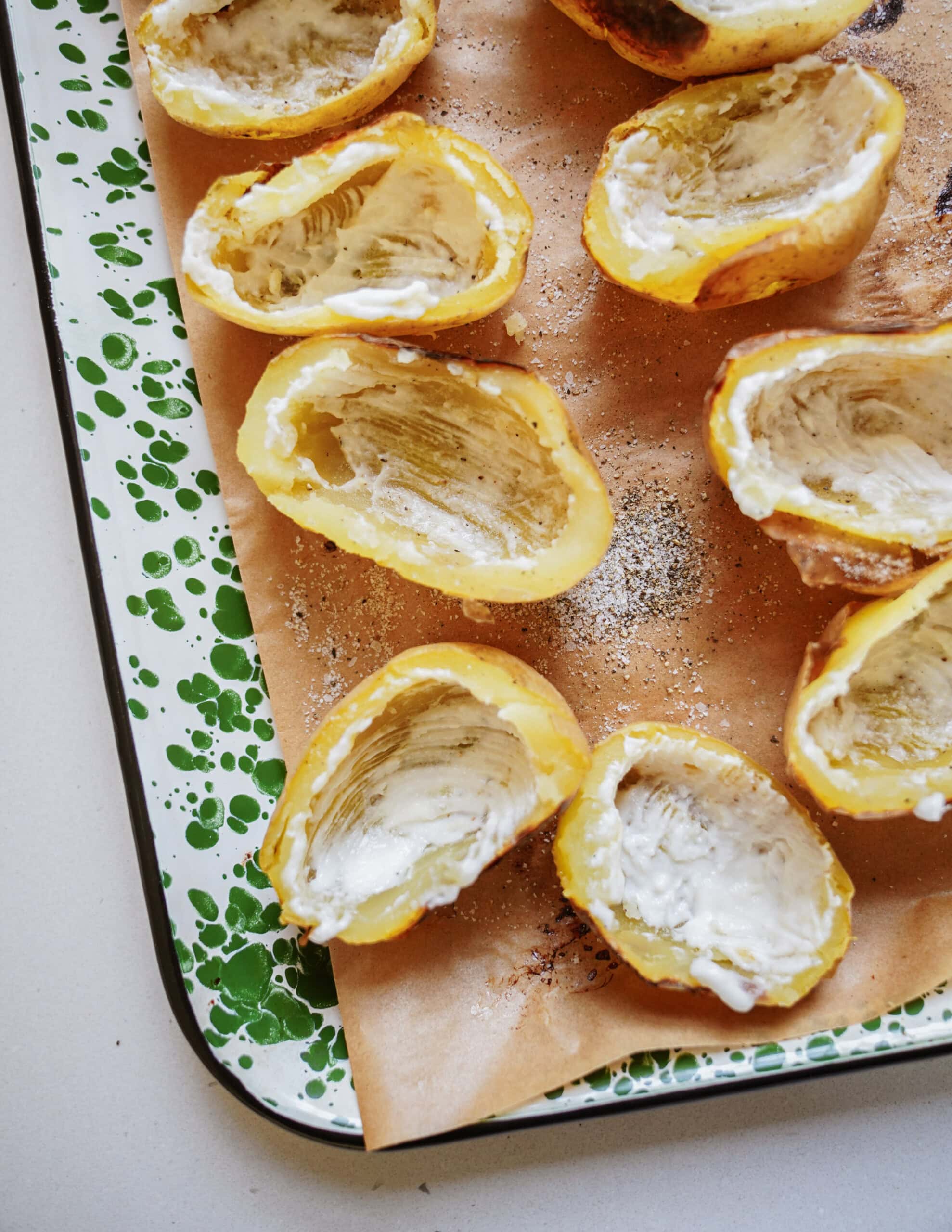 Halved spaghetti squash with the insides scooped out and coated with a creamy spread, arranged on parchment paper on a speckled green and white baking sheet. - 5