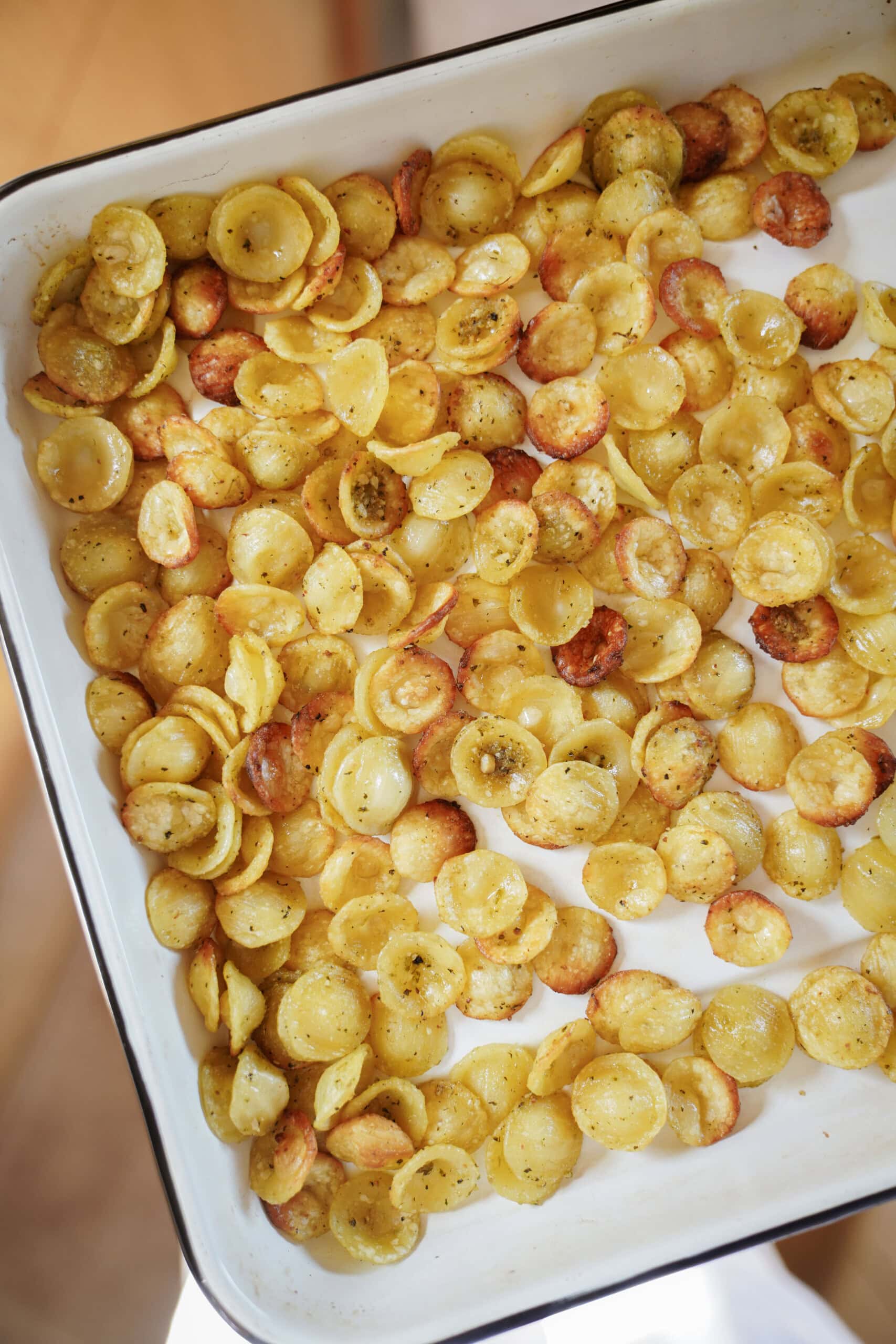 A white baking dish filled with baked orecchiette pasta, seasoned and lightly browned, spread evenly across the surface.