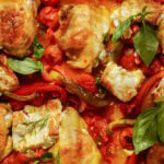 Roasted chicken thighs with tomatoes, red peppers, and chunks of cheese, garnished with fresh basil and dill.