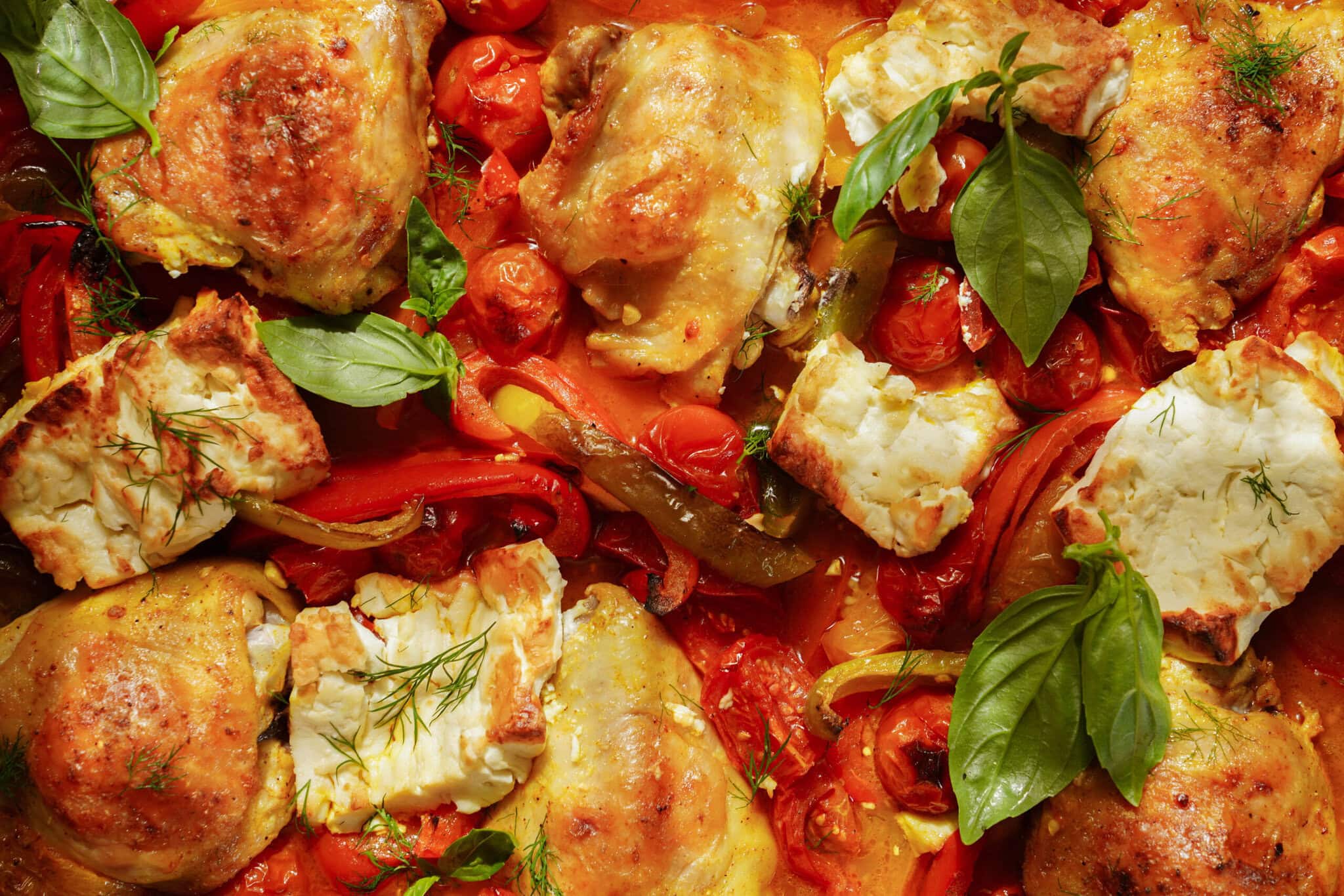Roasted chicken thighs with tomatoes, red peppers, and chunks of cheese, garnished with fresh basil and dill.