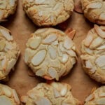 Top-down view of several round, golden almond cookies on parchment paper.