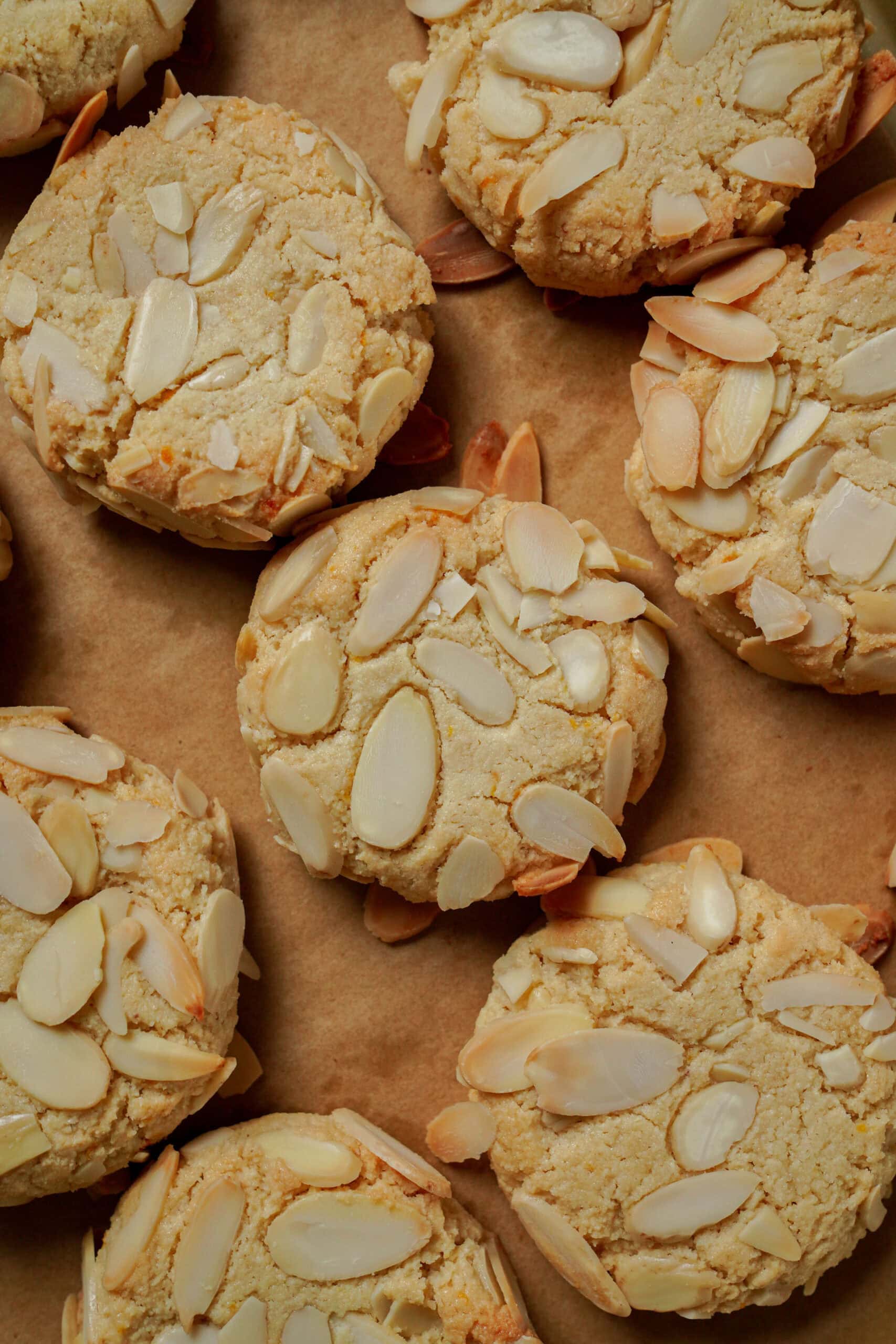 Several round almond cookies topped with sliced almonds on parchment paper.