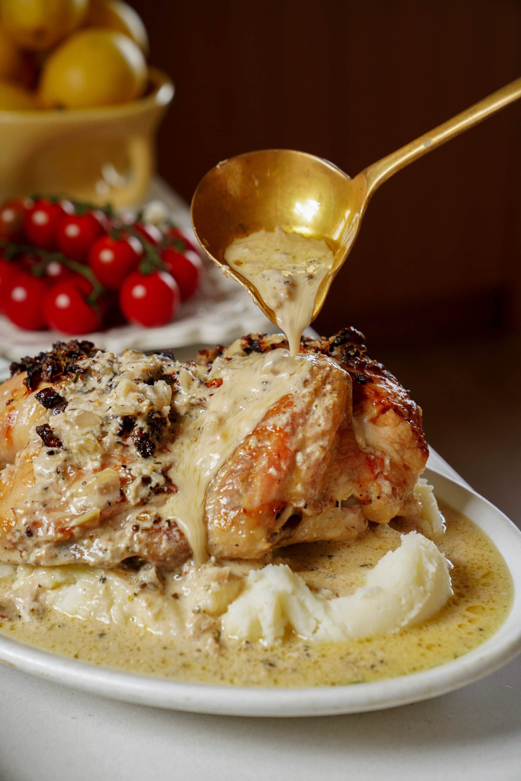 A gold ladle pours creamy sauce over a roasted chicken served on a bed of mashed potatoes.