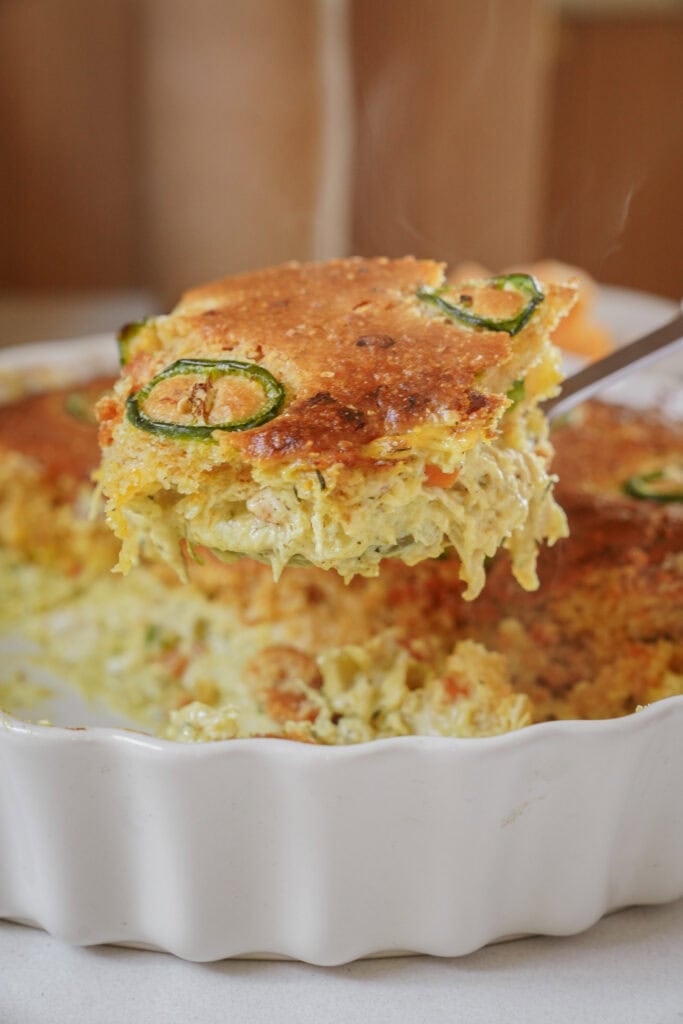 A spatula lifting a serving of jalapeño cornbread casserole from a white baking dish.