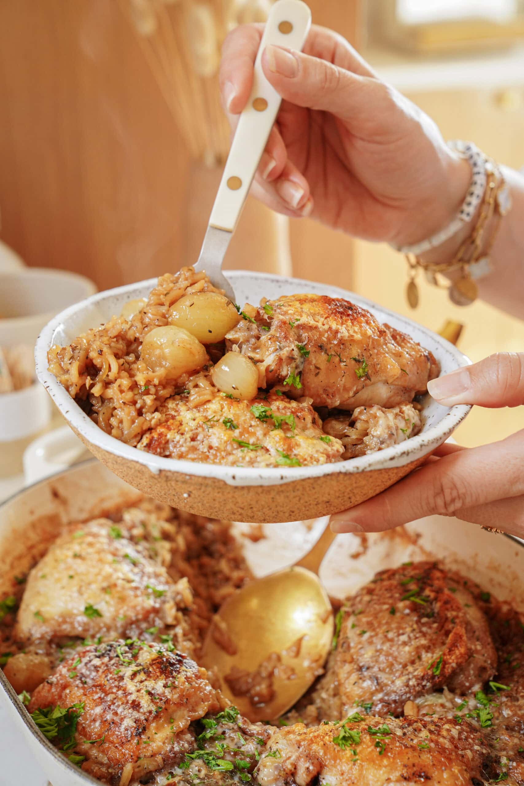 A person holds a small bowl filled with chicken and rice over a larger baking dish of the same meal.