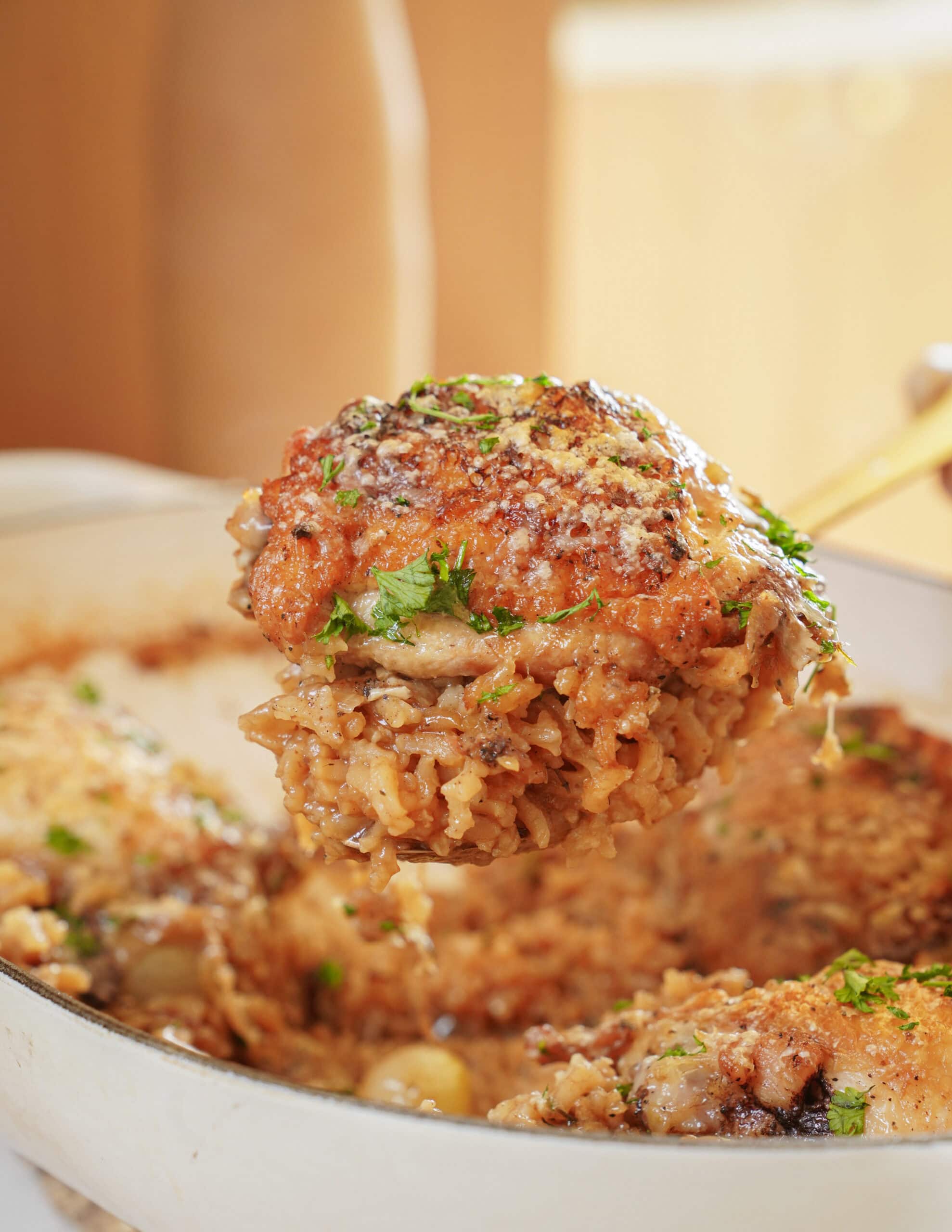 A spoonful of crispy, herb-topped chicken and rice held over a baking dish.