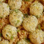 A close-up of several cooked meatballs sprinkled with fresh dill, resting on a bed of rice and sautéed onions.