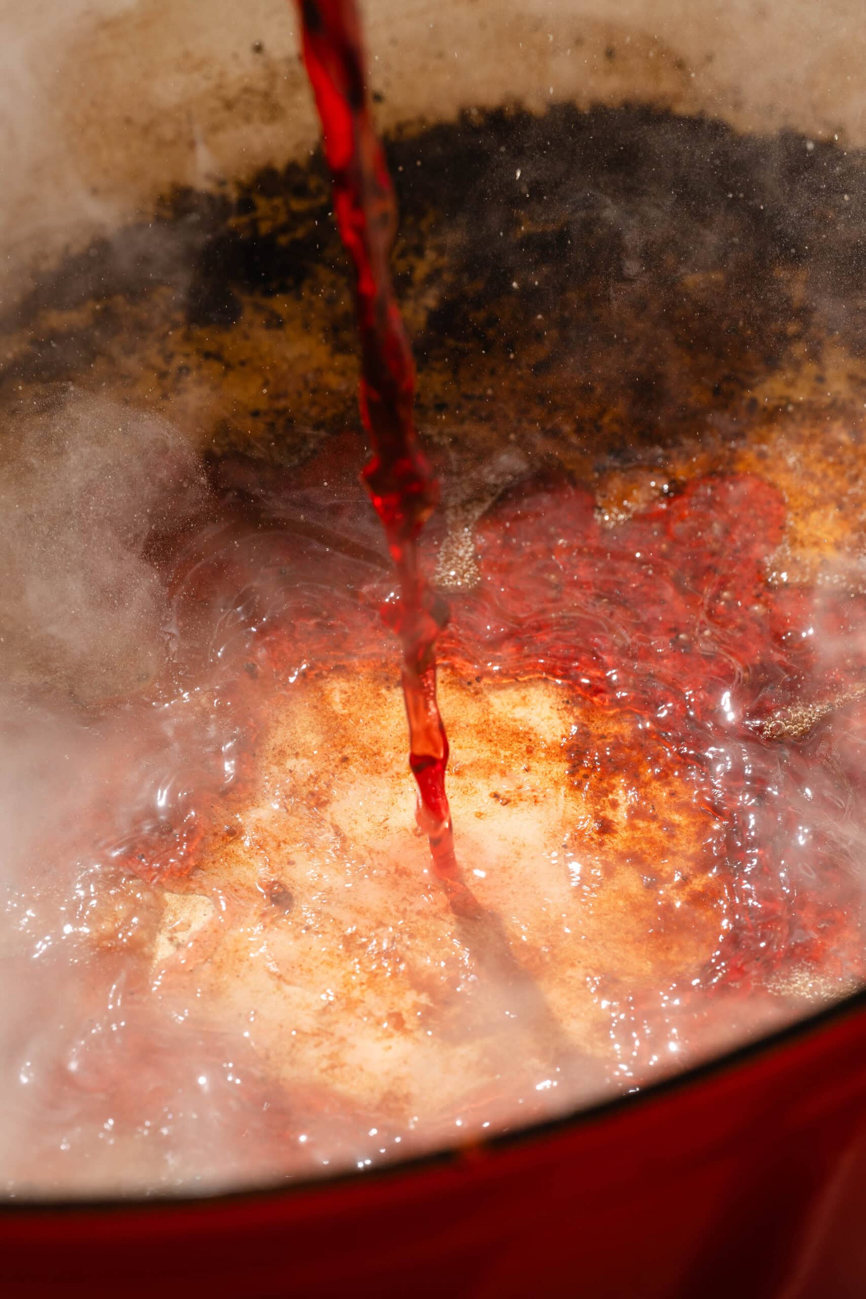 Red wine being poured into a steaming, hot pan.