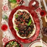 Braised beef short ribs served over a bed of creamy purée, topped with pomegranate seeds, chopped pistachios, and fresh mint on a red platter.